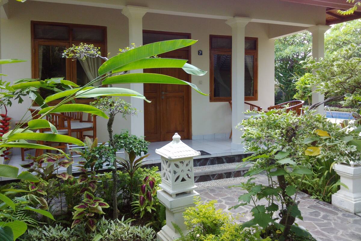 Una casa con porche, piscina y diversas plantas.