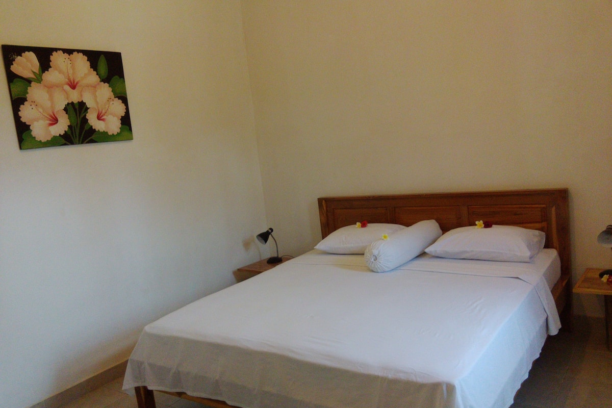 Una cama bien tendida con sábanas y almohadas blancas, un cabecero de madera y una mesita de noche con una lámpara.