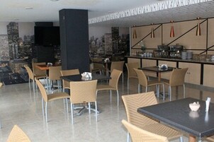 Un restaurante moderno con sillas y mesas de mimbre, vistas a la ciudad y una zona de bar con equipo de cocina.