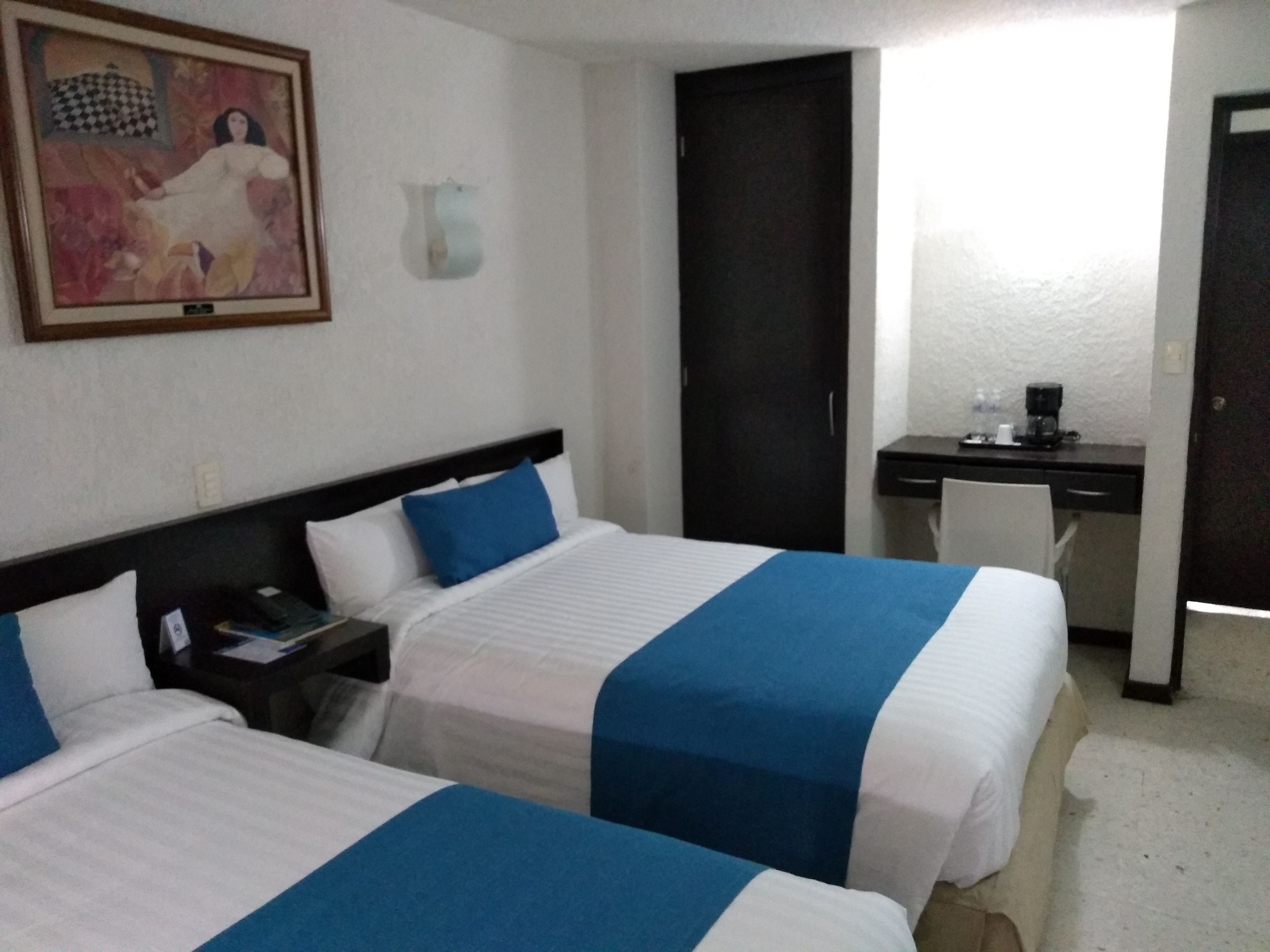 Une chambre d’hôtel avec deux lits, un bureau, une chaise, un tableau et une porte.