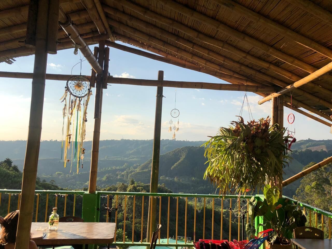 A rustic outdoor seating area with a view of a hilly landscape, bamboo structures, and hanging dreamcatchers.