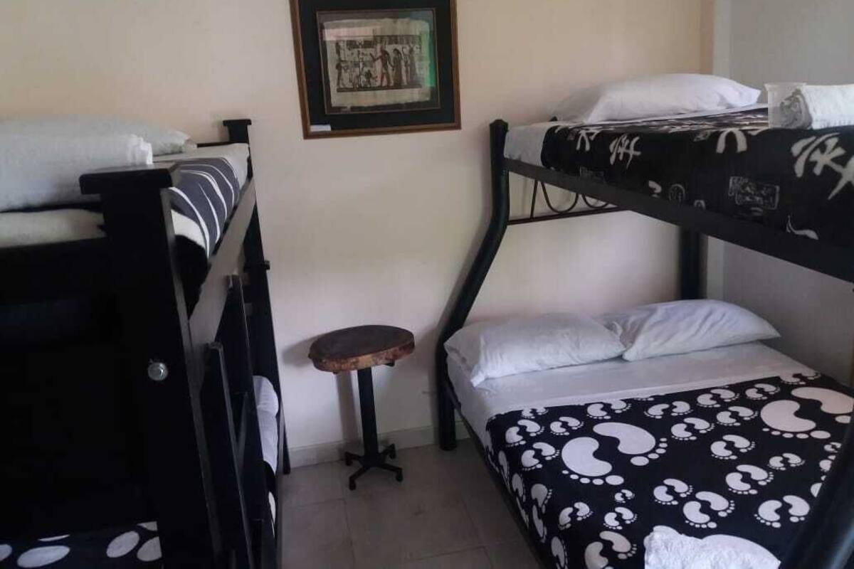 Ein Schlafraum mit Etagenbetten, einem kleinen Hocker und einem gerahmten Bild an der Wand.