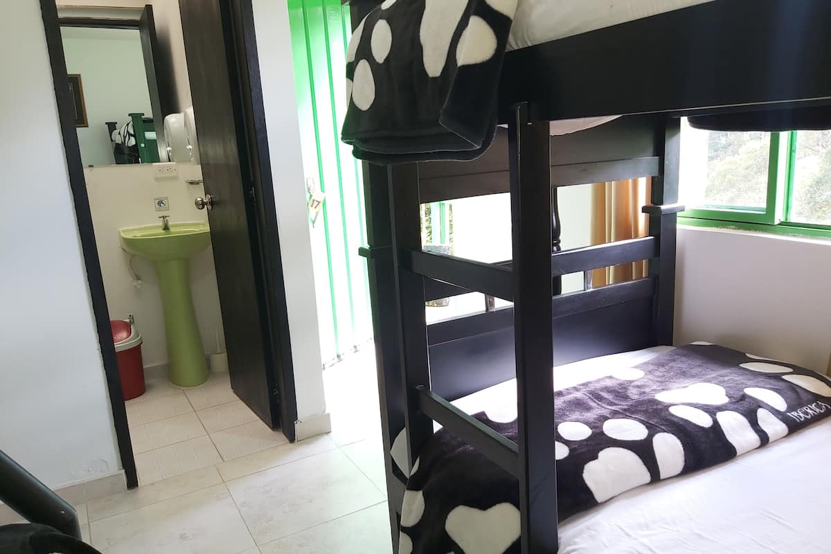 Ein Stockbett mit schwarz-weißer Punkteoptik, ein grünes Waschbecken und ein Spiegel in einem Raum mit gefliestem Boden.