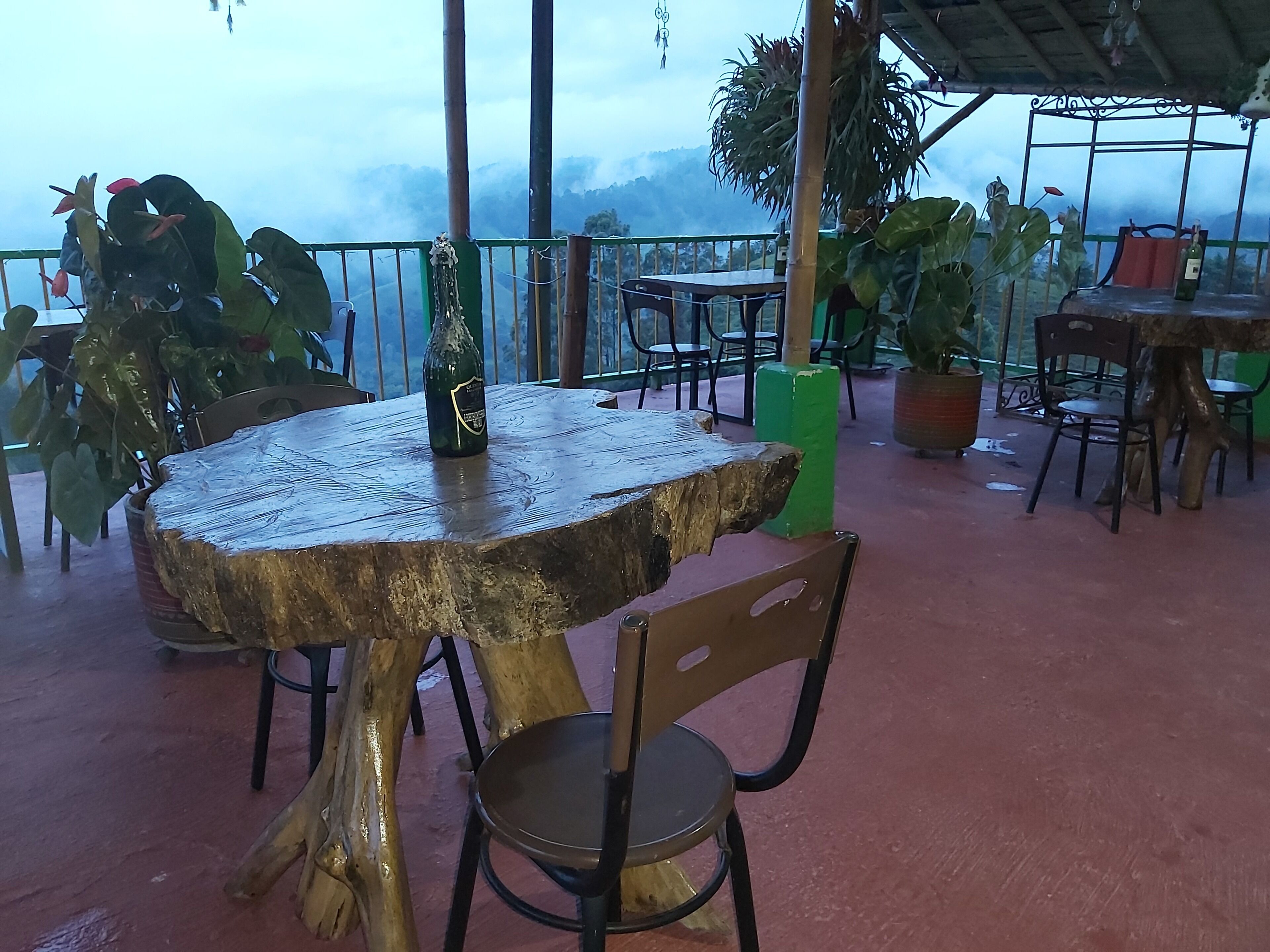 Un espacio de estar al aire libre de estilo rústico con una mesa y sillas de madera, rodeado de plantas en macetas y con vistas a un paisaje montañoso.