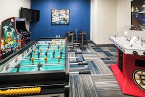 A room with a foosball table, a table tennis table, and a hockey table.