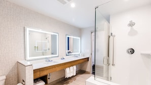 Un baño moderno con ducha de vidrio, tocador de madera con espejo y lavabo blanco.