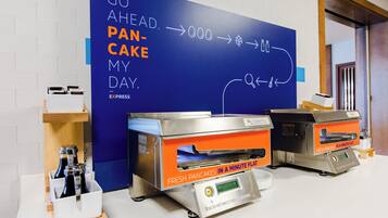 A kitchen area with two pancake-making machines labeled 'Fresh Pancakes in a Minute Flat' and a blue wall with directional arrows and text.