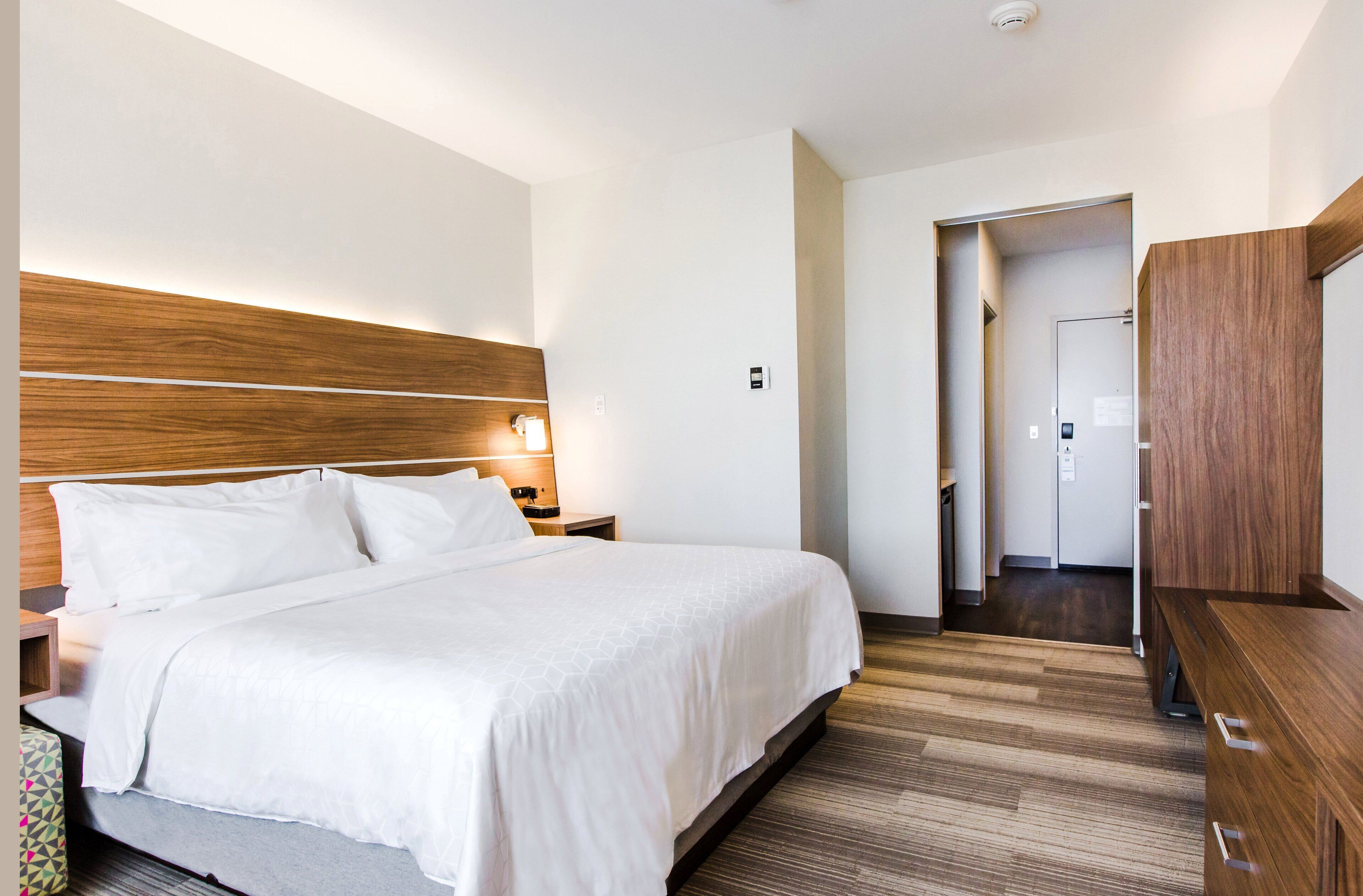A hotel room with a large bed, a wooden headboard, a bedside table with a lamp, and a wooden desk.