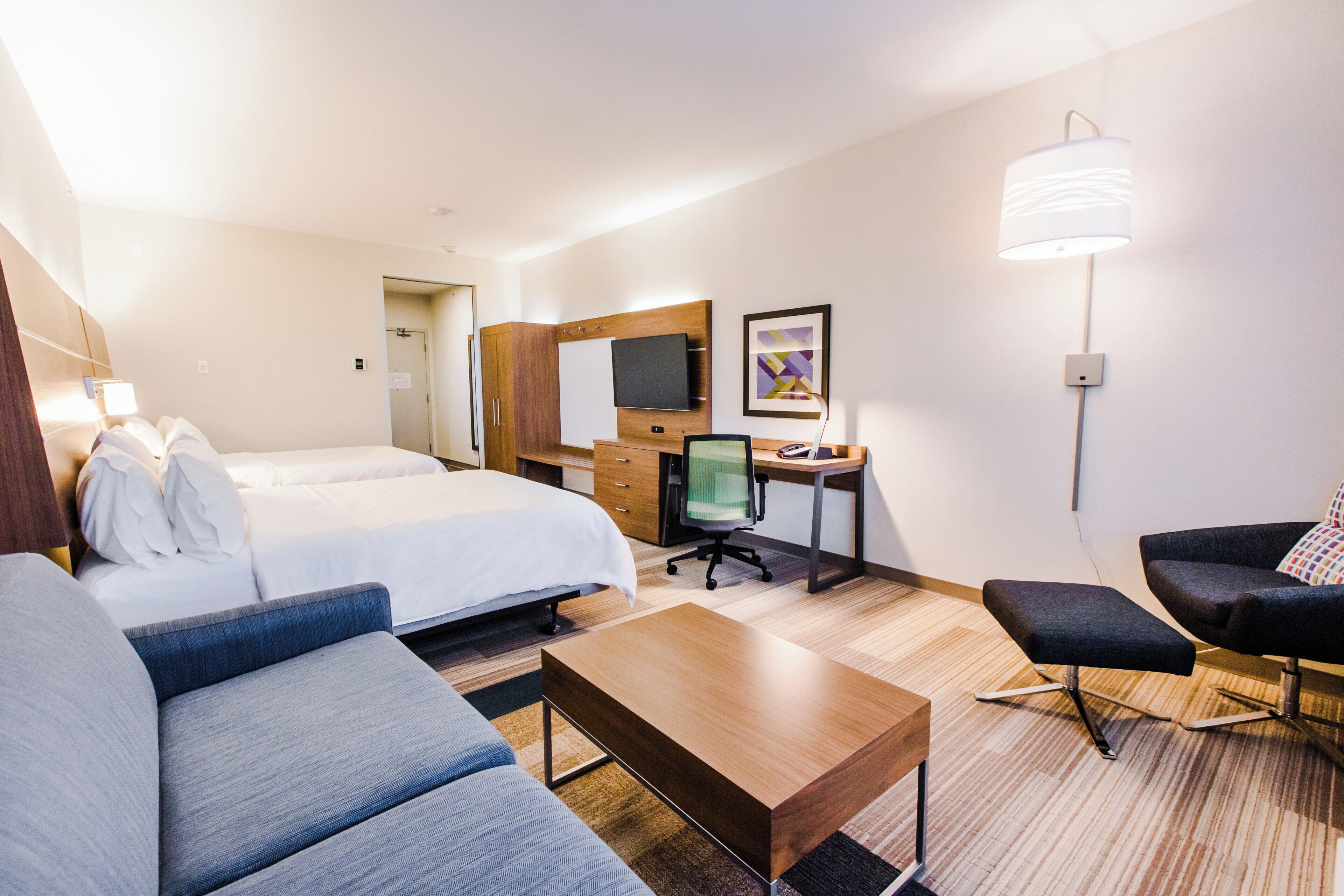 A hotel room with a bed, a desk, a chair, a sofa, and a lamp.