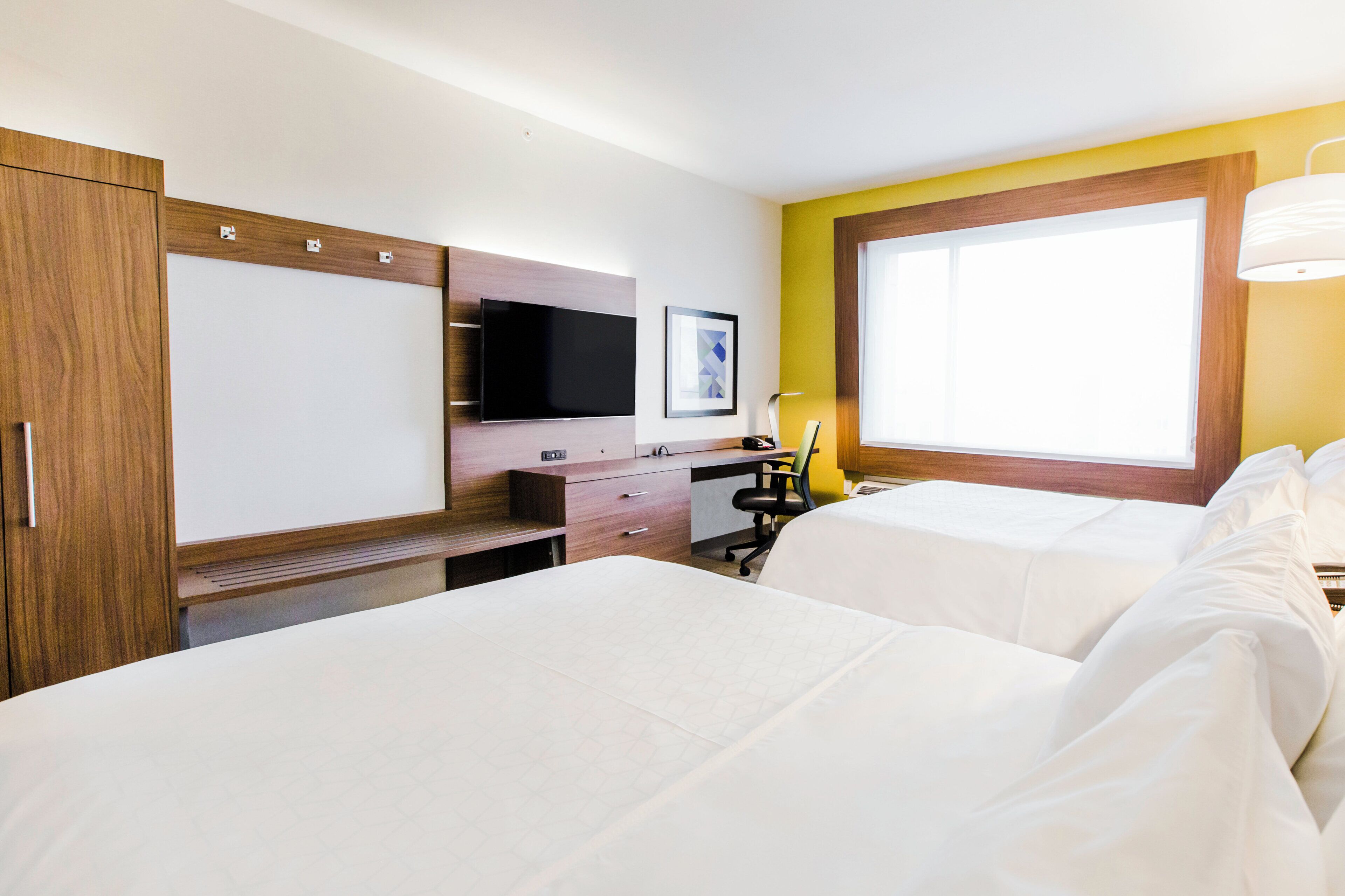 Een hotelkamer met twee bedden, een bureau met stoel, een televisie en een raam.