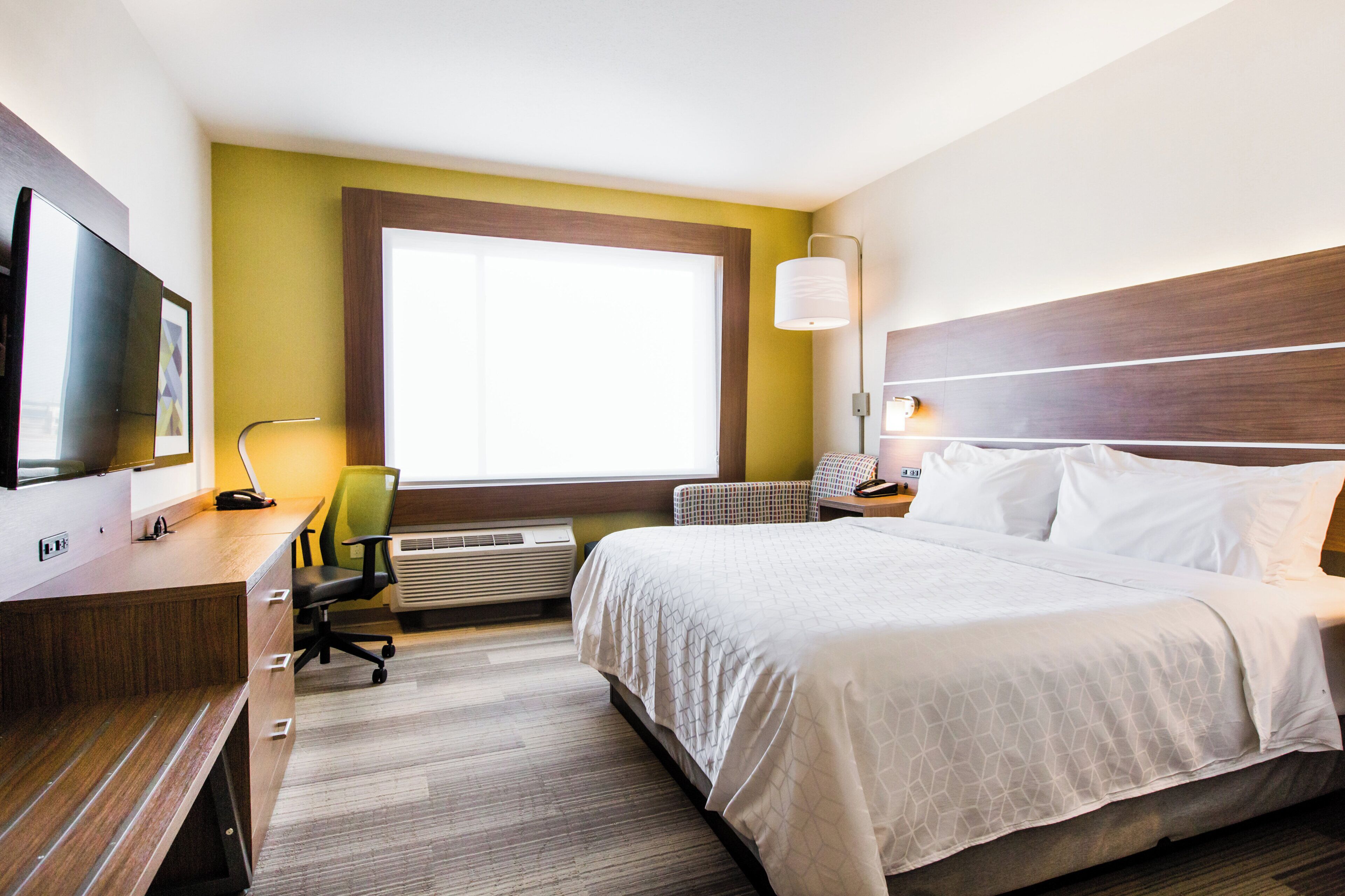 A hotel room with a bed, desk, chair, television, and a window with a view.