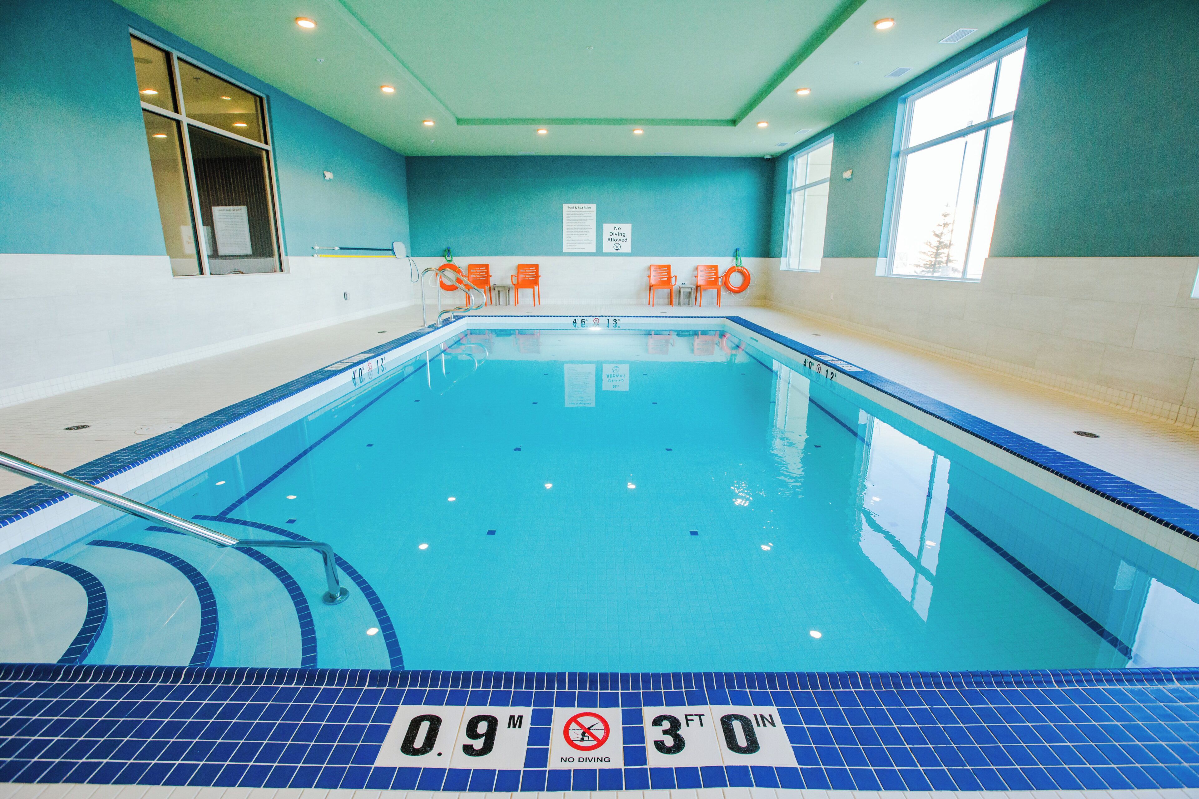 An indoor swimming pool with clear lane markings, safety signs, and a lifeguard chair.
