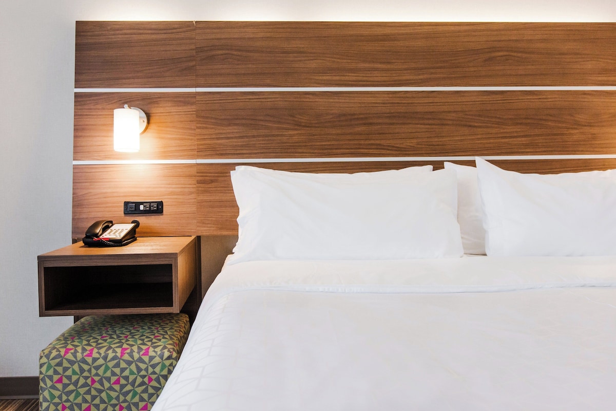 A hotel room with a wooden headboard, a bedside table with a telephone, and a patterned bench.