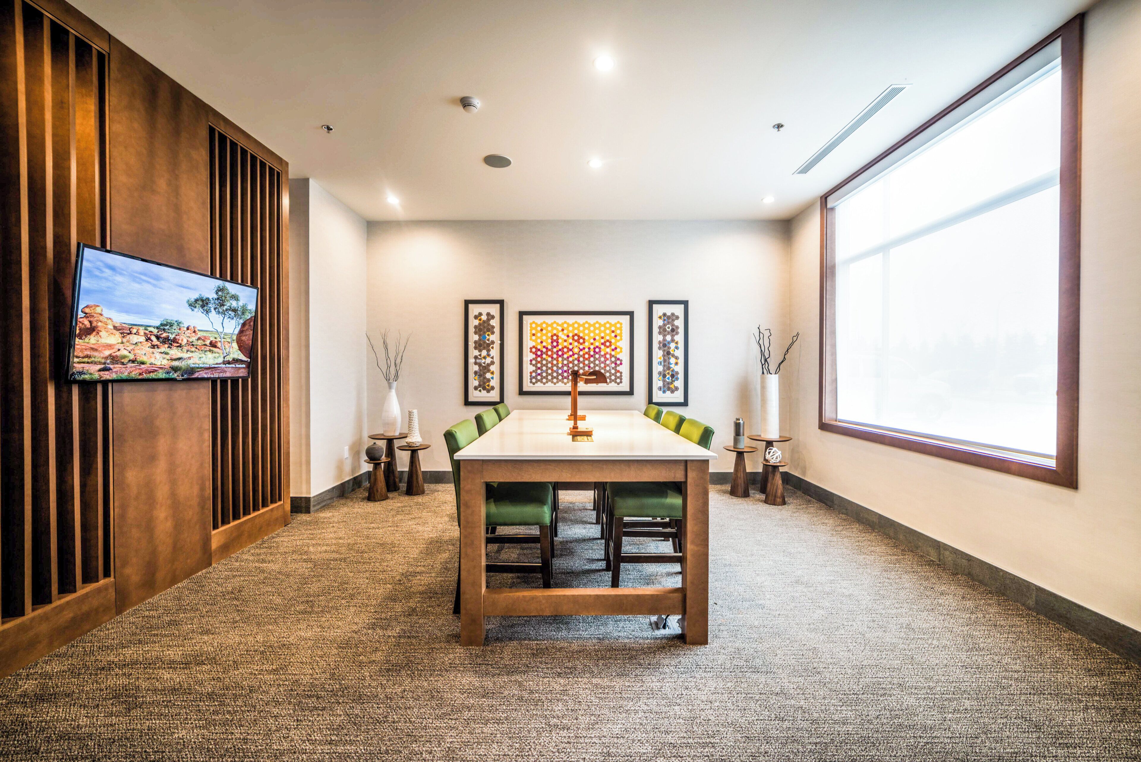 Een vergaderzaal met een grote tafel, stoelen, een televisie, ingelijste kunstwerken en een projectiescherm.