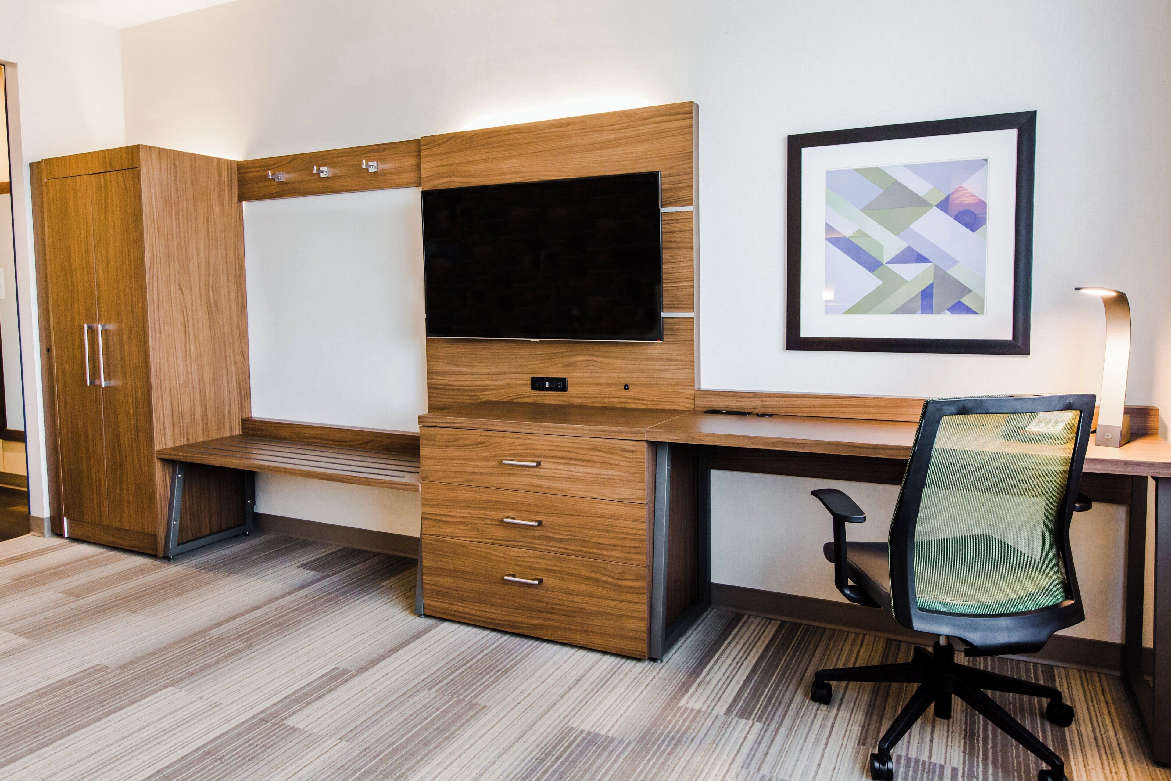 A modern office space with a desk, chair, television, and storage cabinets.