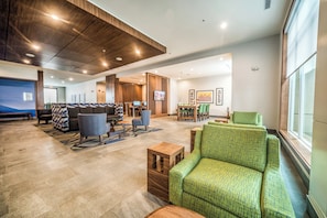 Un hall d’entrée spacieux avec un plafond haut, un coin salon avec des canapés et des fauteuils, un téléviseur fixé au mur et un coin repas avec une table et des chaises.