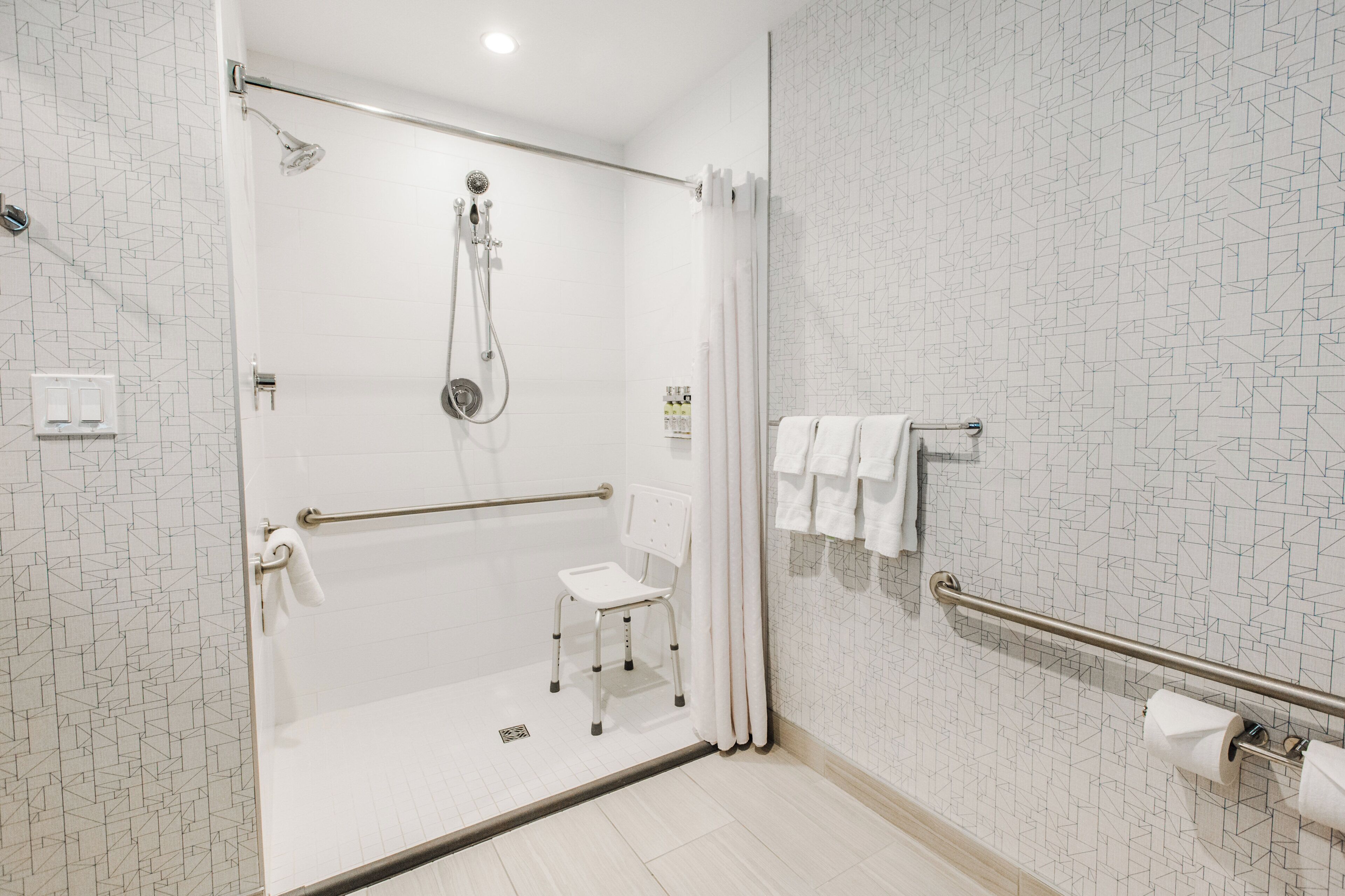 A modern bathroom with a shower, a white toilet, and a grab bar.
