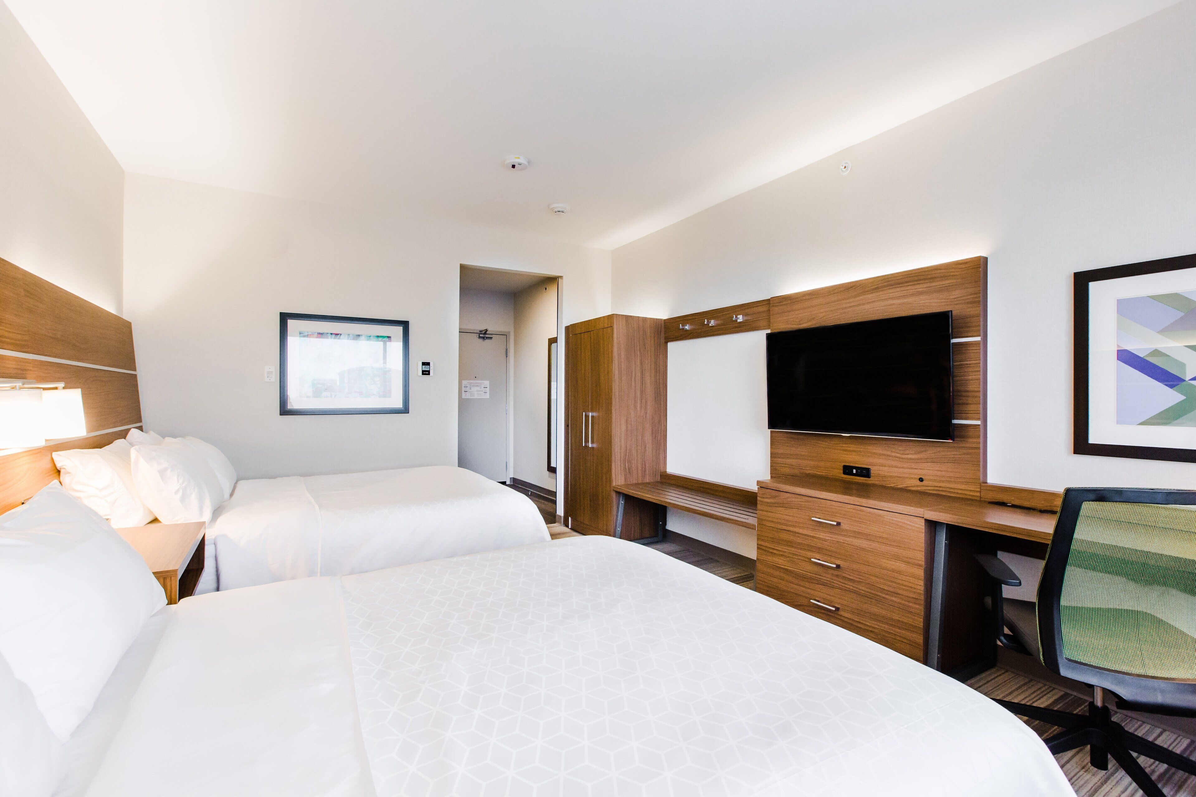 Une chambre d’hôtel avec deux lits, un bureau, une chaise, une télévision et un tableau encadré au mur.