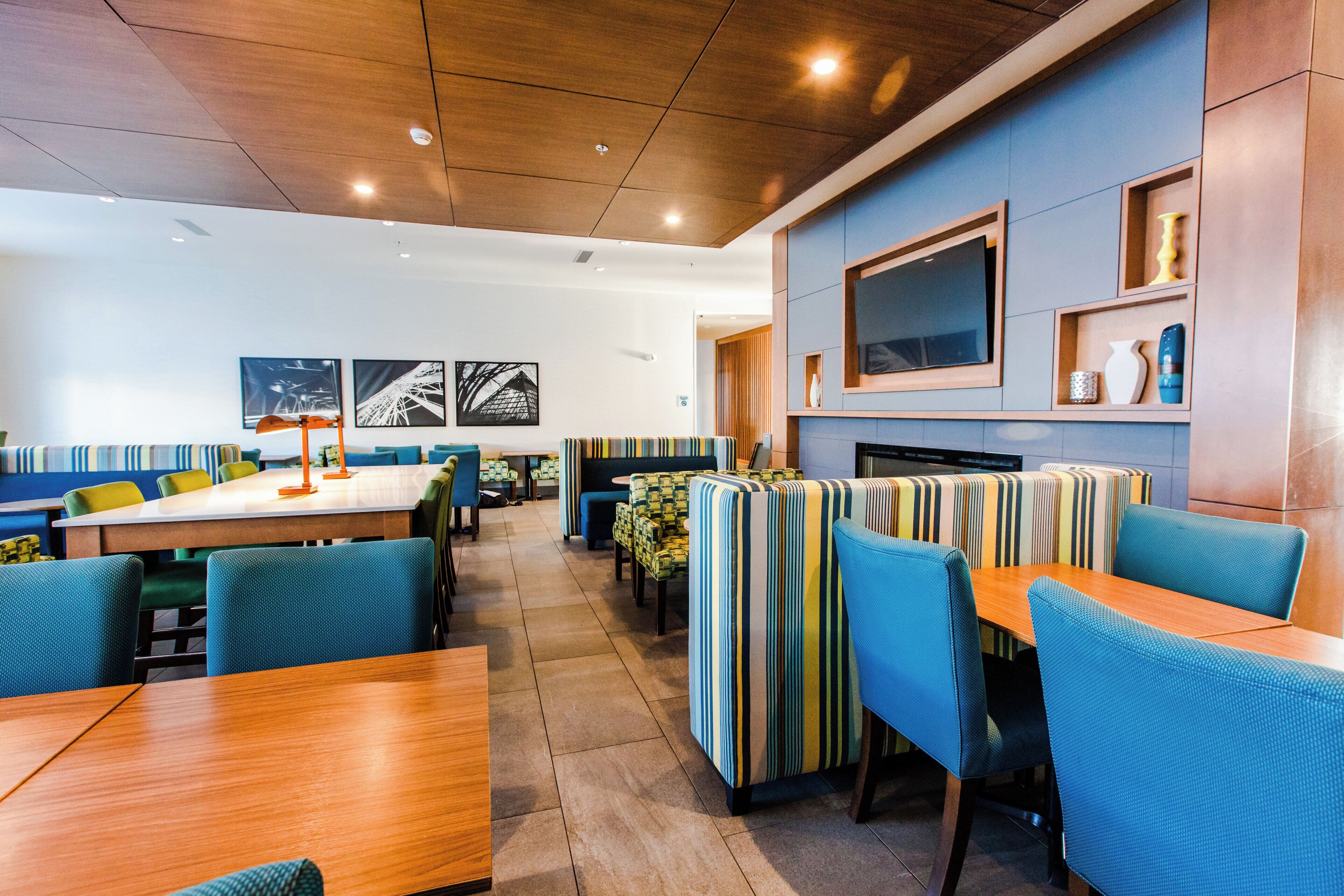 A modern restaurant interior with booths and tables, a flat-screen TV mounted on the wall, and artwork on the walls.