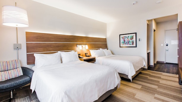 Habitación de hotel con dos camas, un sofá, una lámpara, una mesita de noche y un cuadro en la pared.