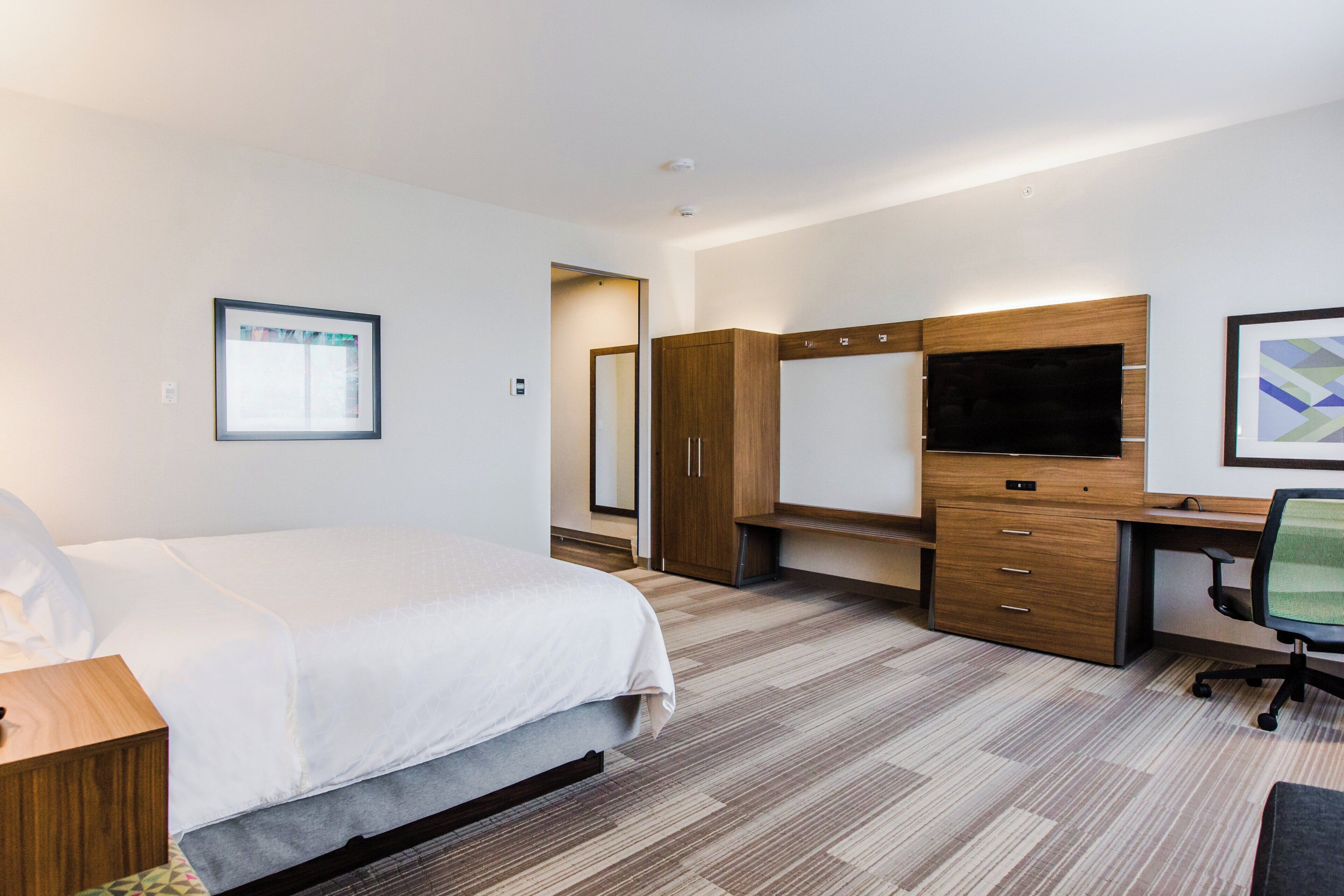 A hotel room with a bed, a desk with a chair, a TV, and a wardrobe.