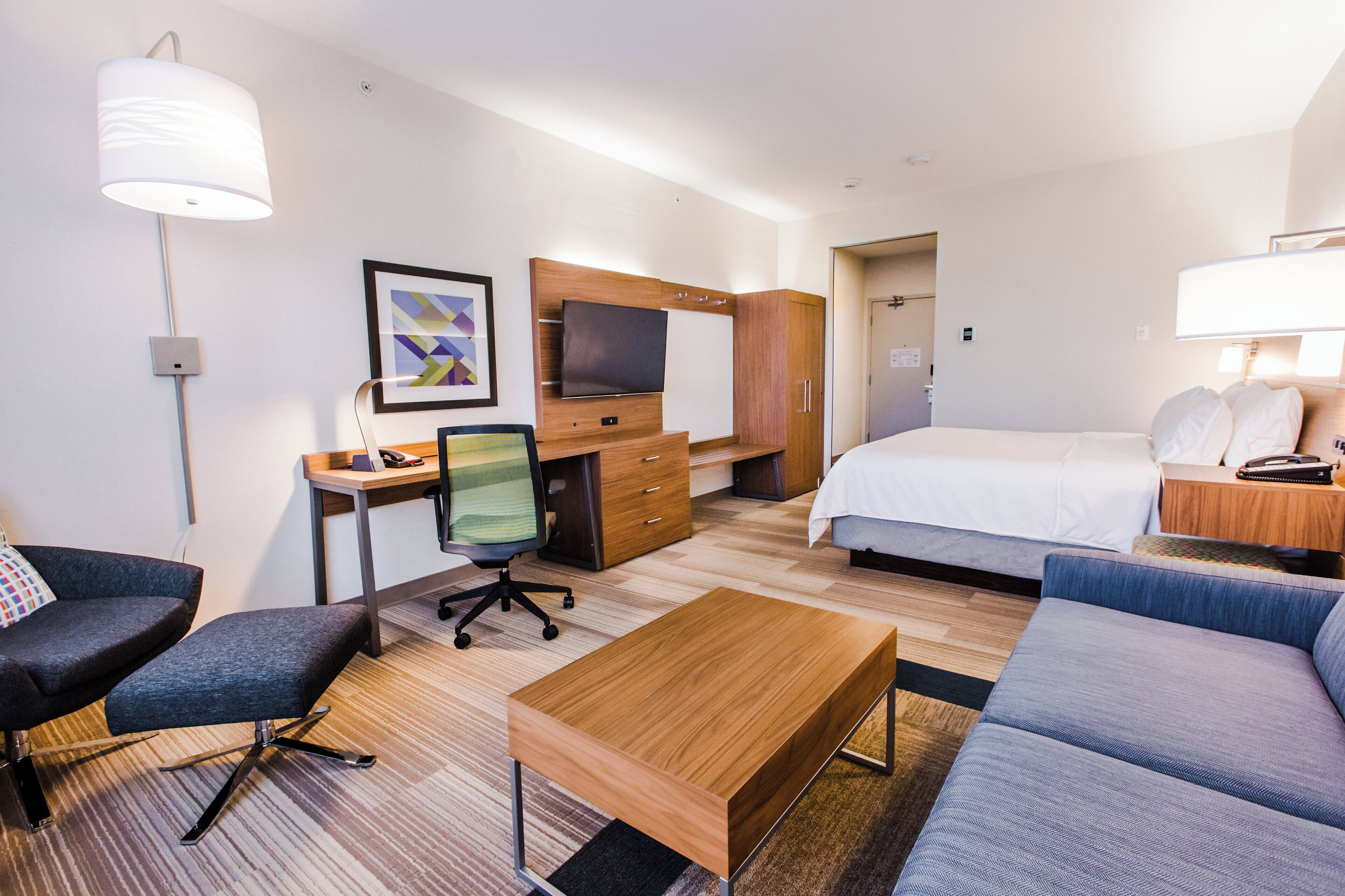 A hotel room with a bed, a desk with a computer, a chair, a sofa, and a TV.