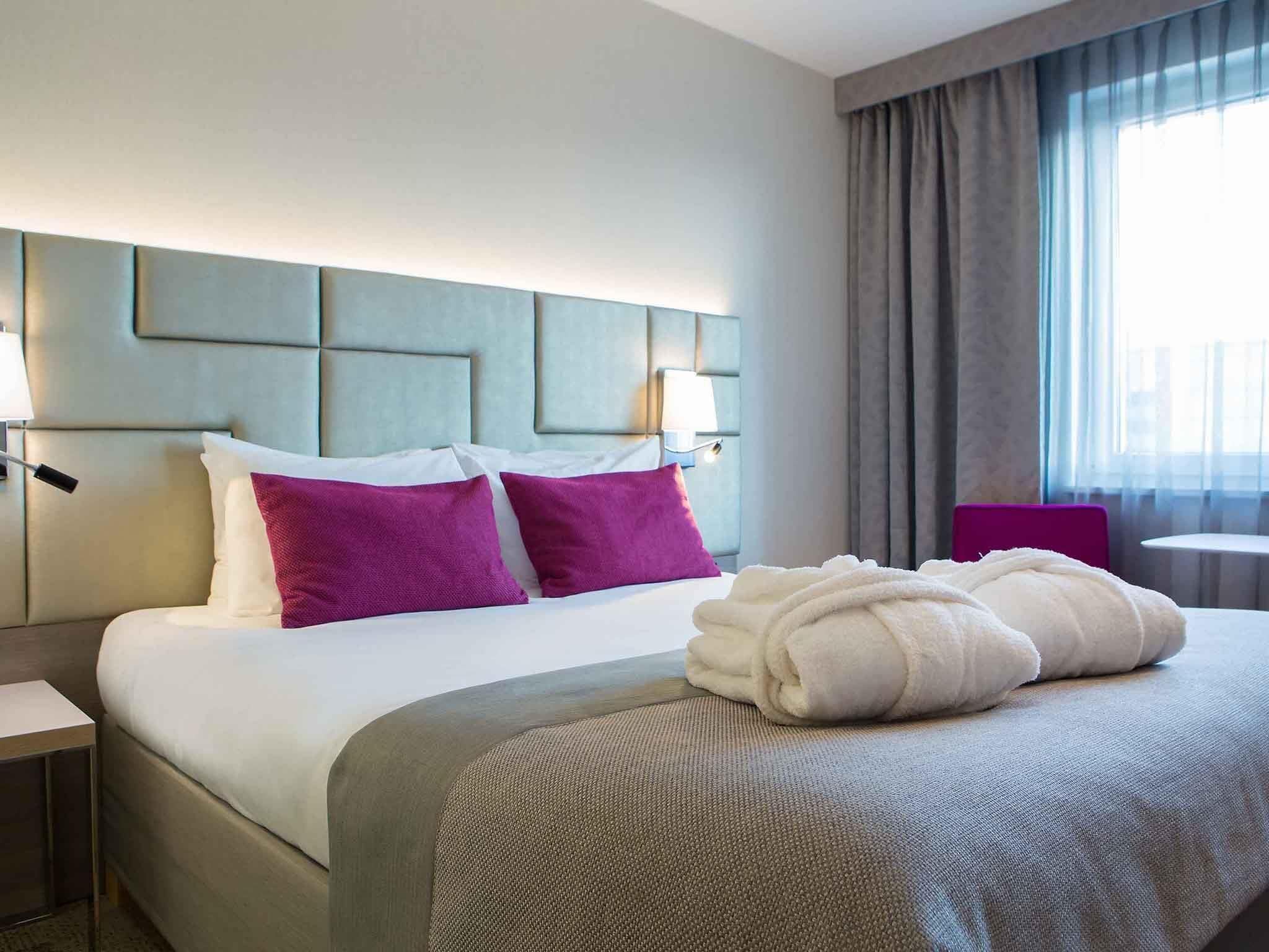 Une chambre d’hôtel avec un lit, une table de chevet, une lampe et une fenêtre avec des rideaux.