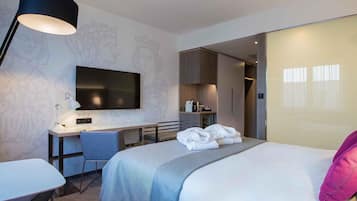 A modern hotel room with a bed, desk, chair, and a flat-screen TV.