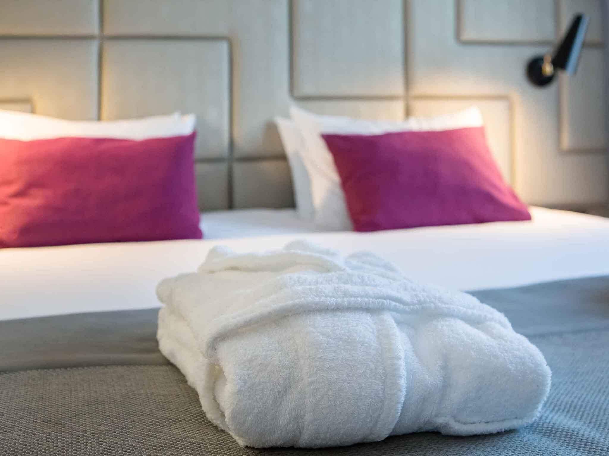A neatly made bed with white and pink pillows, a white towel, and a grey headboard.
