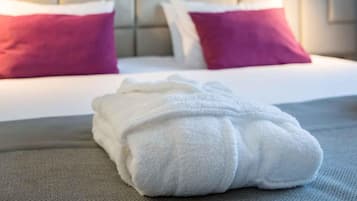 A neatly made bed with white and pink pillows, a white towel, and a grey headboard.