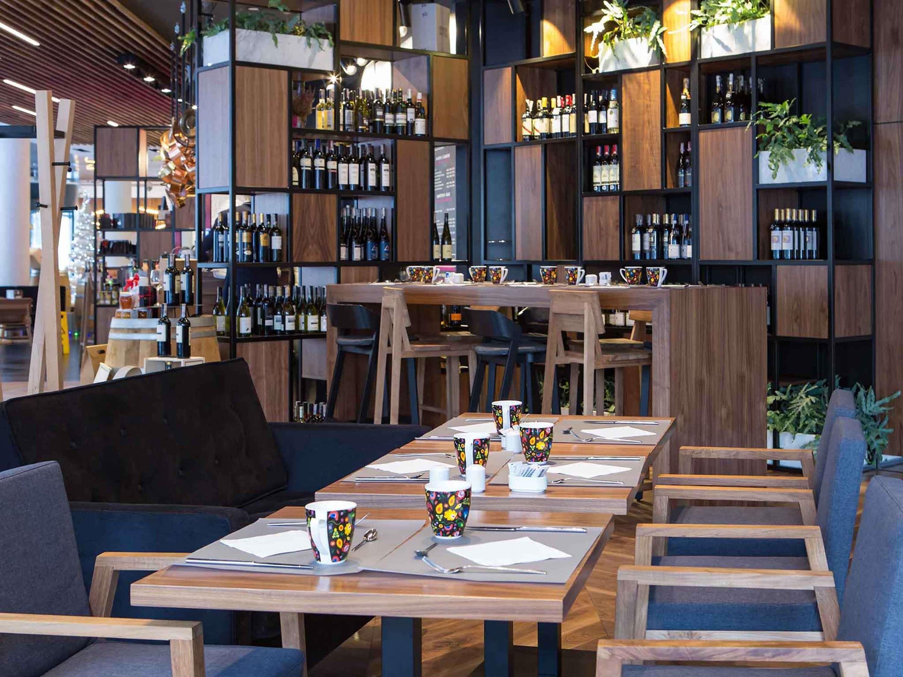 A modern bar area with wooden shelves stocked with bottles, a long table with chairs, and decorative plants.