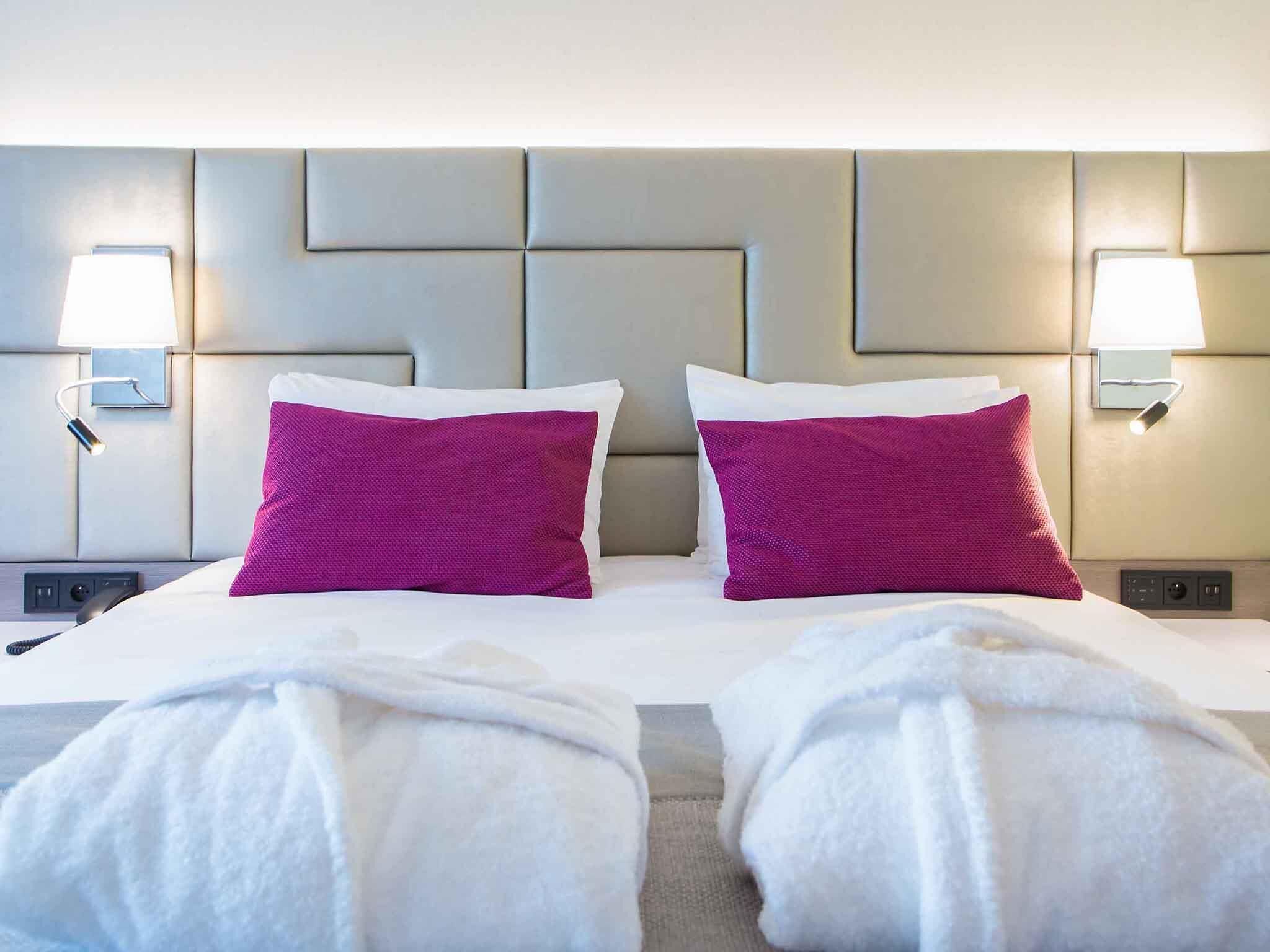 A hotel room with a large bed, two pillows, bedside lamps, and a headboard with a geometric design.
