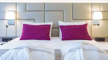 A hotel room with a large bed, two pillows, bedside lamps, and a headboard with a geometric design.
