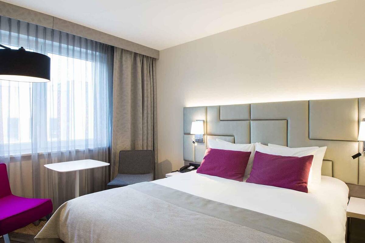 Une chambre d’hôtel avec un grand lit, un bureau, une chaise et une fenêtre avec des rideaux.
