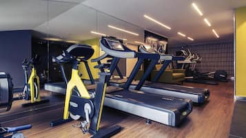 Un gimnasio con equipamiento de ejercicio, incluyendo cintas de correr y una elíptica, con suelo de madera y un espejo grande.