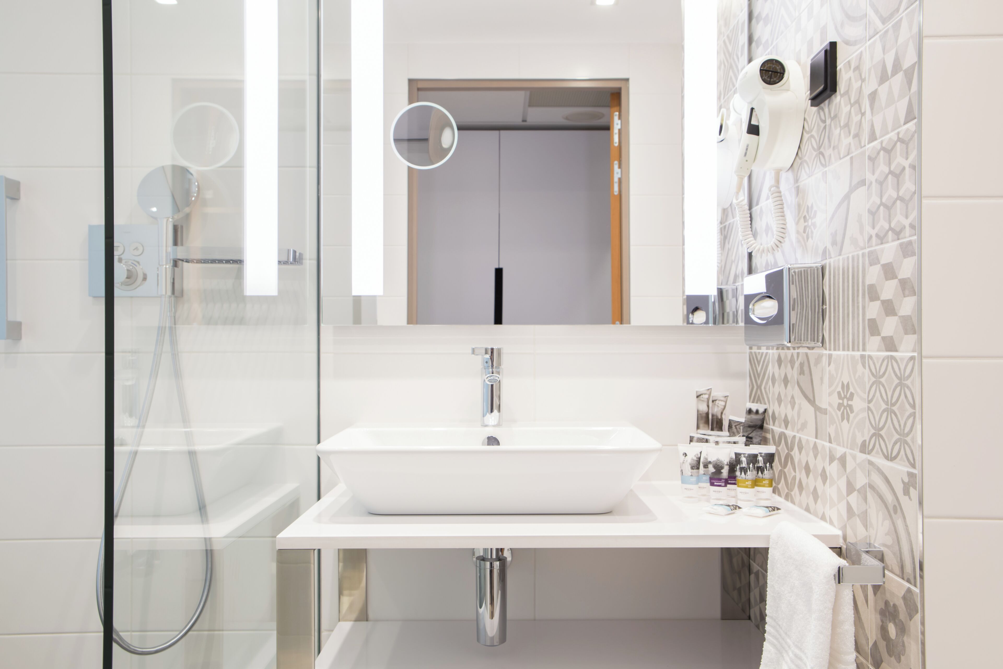 A modern bathroom with a glass shower enclosure, a white sink, and a mirror above it.
