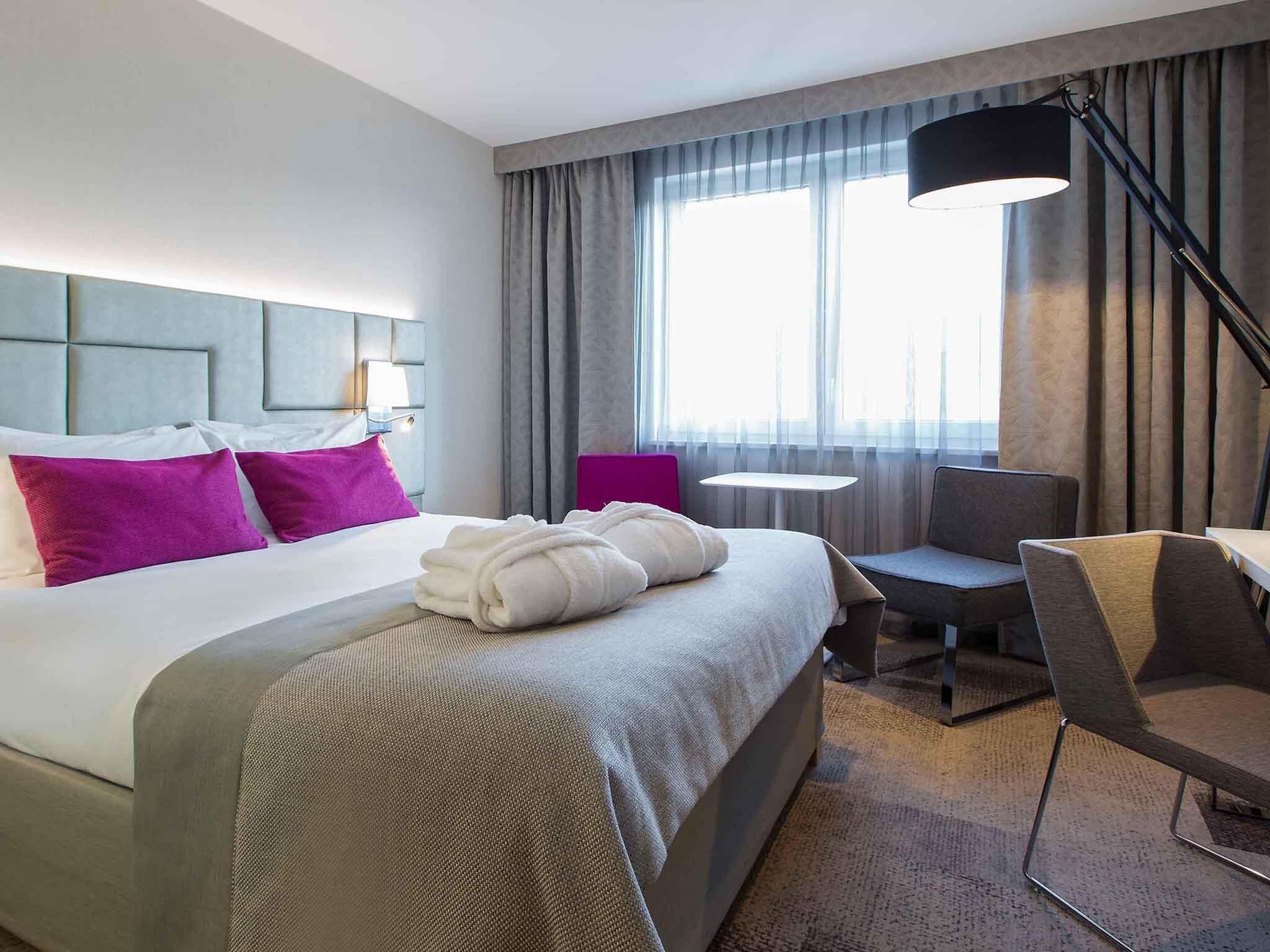 Een hotelkamer met een groot bed, een bureau, een stoel, een lamp en een raam met gordijnen.