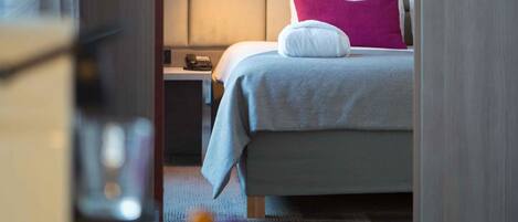 Una habitación de hotel con cama, mesita de noche, lámpara y teléfono en la pared.
