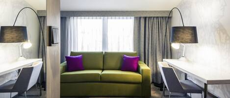 Ein modernes Hotelzimmer mit einem grünen Sofa, zwei Schreibtischen und zwei Lampen.