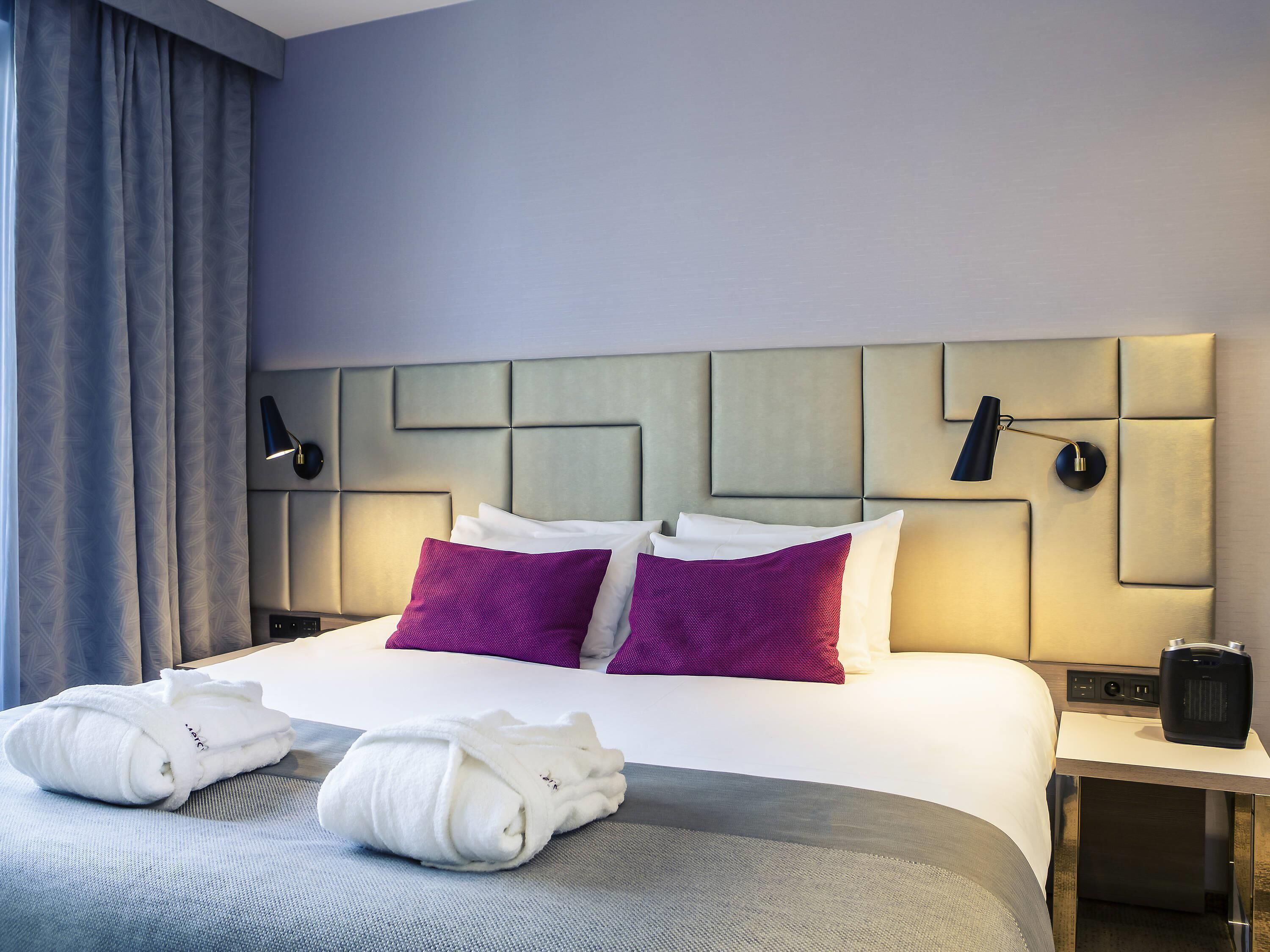 A hotel room with a bed, pillows, a nightstand, a lamp, and a towel.