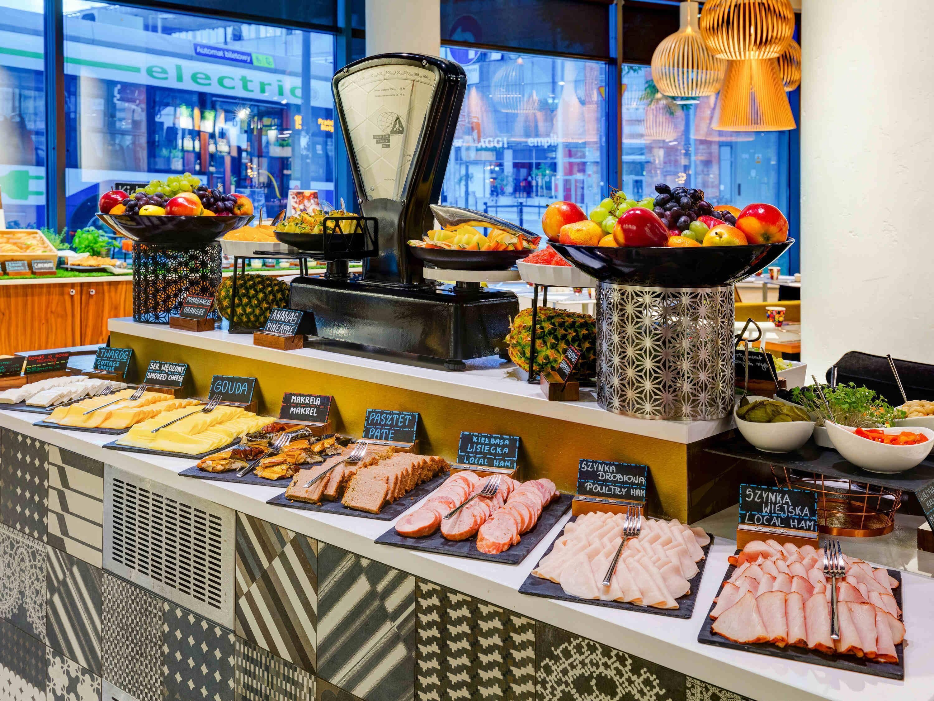 A buffet with various food options, including fruits, cheeses, meats, and a coffee machine.