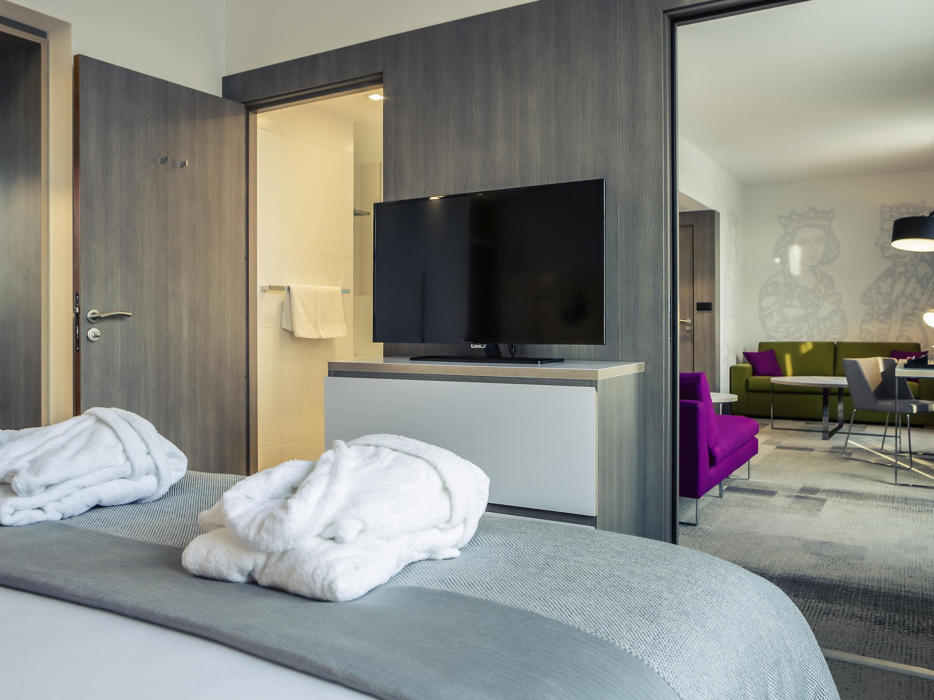 A hotel room with a bed, a TV, a desk, and a seating area with a couch and chairs.