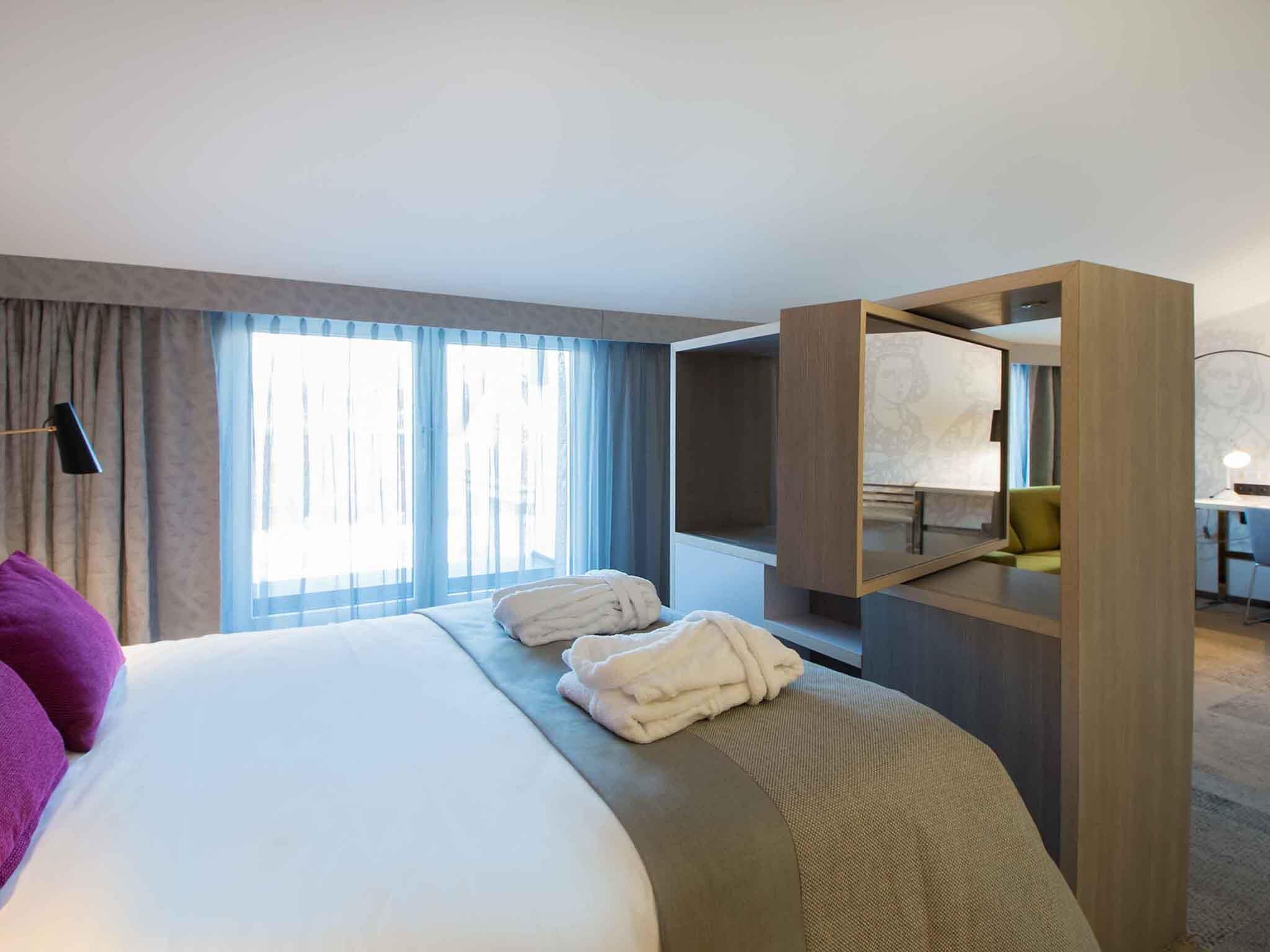 A hotel room with a large bed, a desk, and a wardrobe.