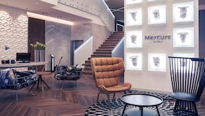 A modern hotel lobby with a curved staircase, a reception desk, and a seating area with a round table and chairs. - Mercure Krakow Stare Miasto (Old Town) (Kraków)