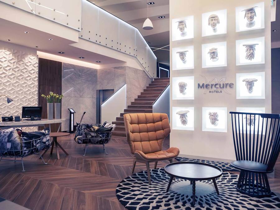 Un hall d’hôtel moderne avec un escalier en colimaçon, un comptoir d’accueil et un espace détente comprenant une table ronde et des chaises.