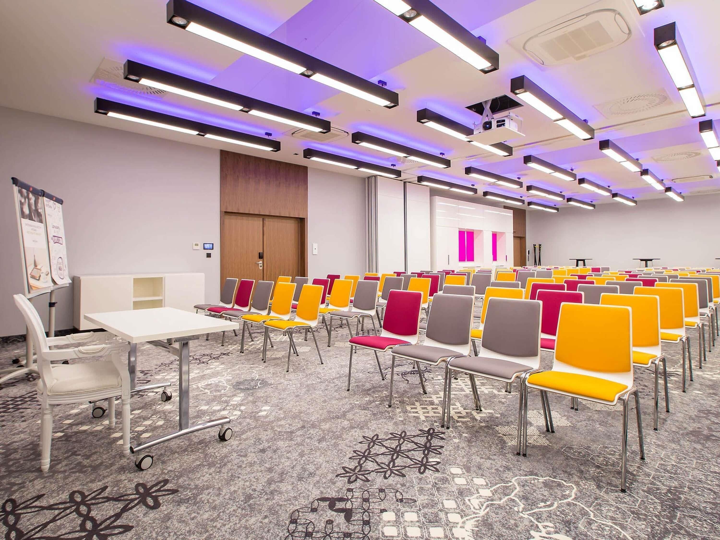 A conference room with rows of chairs, a white table, and a carpeted floor.