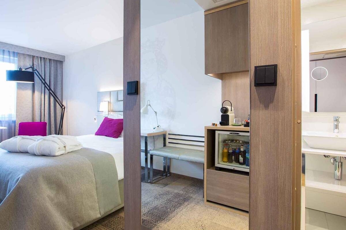 Une chambre d’hôtel moderne équipée d’un lit, d’un bureau et d’un mini-bar intégré.