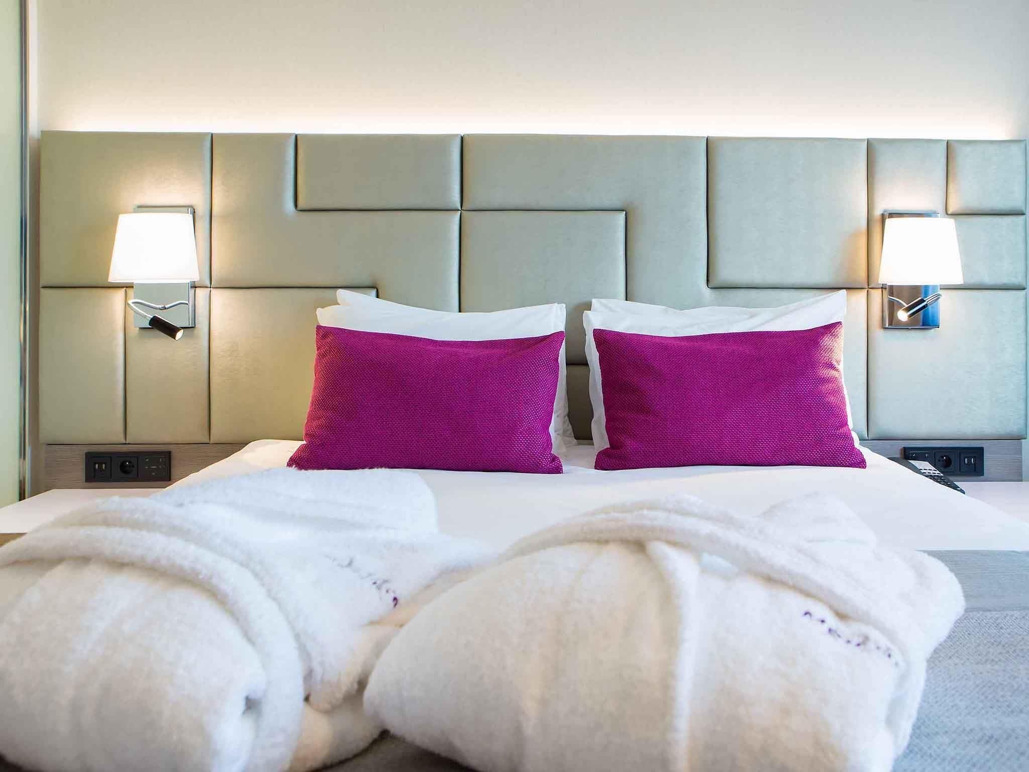 Une chambre d’hôtel avec un lit, deux oreillers, deux lampes fixées au mur et une tête de lit.