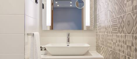 A bathroom with a white sink, a mirror, and patterned tiles.