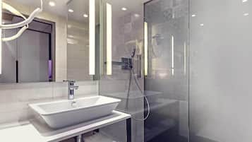 A modern bathroom with a large white sink, a glass shower enclosure, and a mirror with vertical light strips.